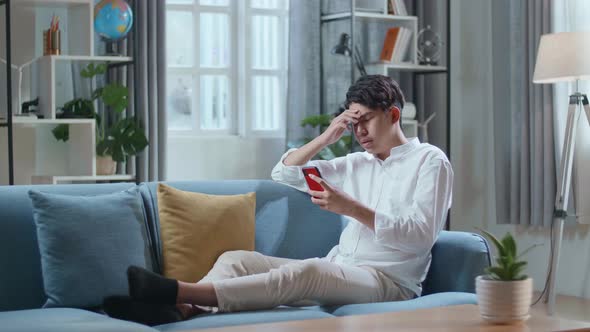 Full Body Of Asian Man Being Tired While While Lying On Sofa And Using Smartphone In The Living Room