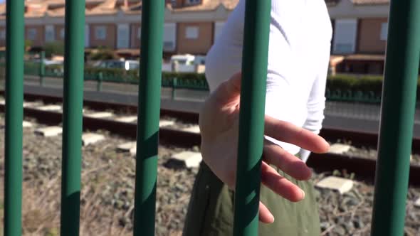 Girl walking and sliding her hand on the railing, in the background houses and train track