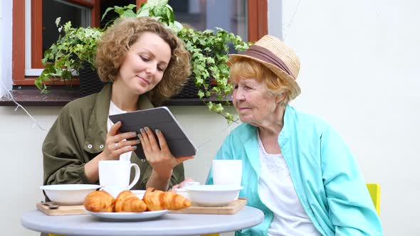 Granddaughter Helping Grandmother With Tablet Computer In Cafe