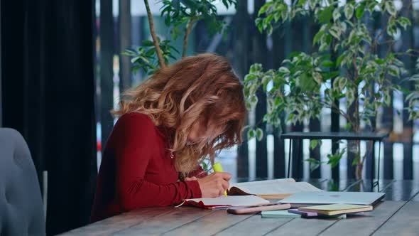 A Young Sad Female Student Overwhelmed with Homework Sits with a Laptop in a Cafe alt