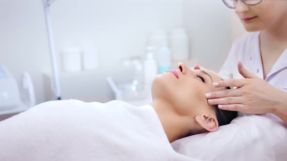 Professional Female Cosmetologist Making Massaging Temple and Face at Beauty Salon