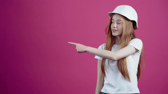 The Young Redhead with the Engineer's Helmet Points with Her Index Finger to One Side and Approves