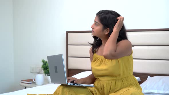 Thoughtful Indian woman working on laptop