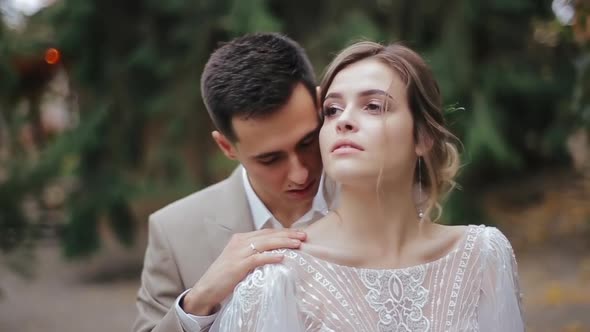 Groom in Suit Kisses on the Shoulder His Beautiful Bride in Dress, and Then at the Temple on Blurry