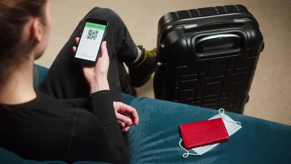 Woman Tourist Holding QR Code on Phone Sitting in Airport Terminal