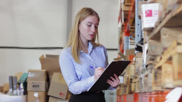 Woman Appearance Notebook Pen Looks at Shelves with Boxes in Warehouse