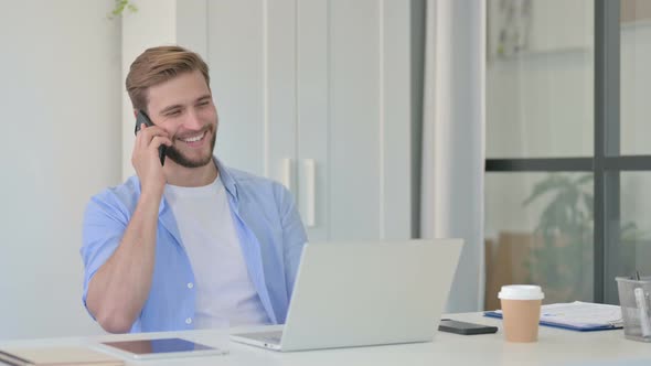 Young Creative Man with Laptop Talking on Smartphone