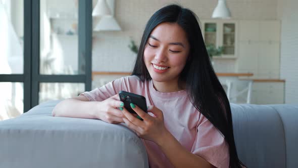 Front View of a Serene Happy Darkhaired Asian Woman Using Her Smartphone for Texting Browsing Mobile