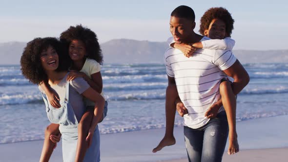 African american mother and father giving a piggyback ride to their daughter and son at the beach