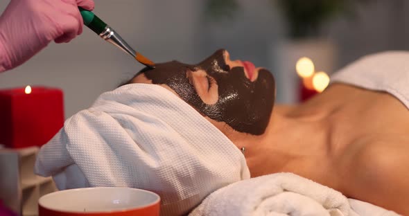 Beautician Applying Dark Clay Mask on Woman Face