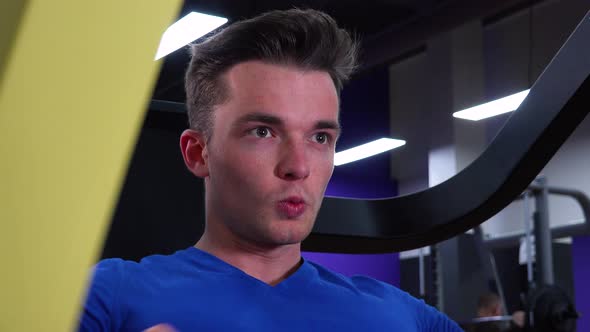 A Young Fit Man Trains on a Machine in a Gym - Face Closeup