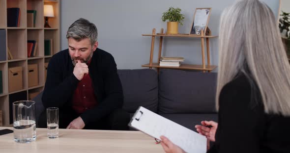 Crop View of Thoughtful Mature Man Sitting on Sofa and Having Therapy Session with Female Person