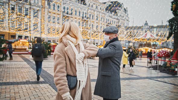 Senior Man and Woman in Protective Masks Greeting Each Other Outdoors Bumping Elbows Walking in City