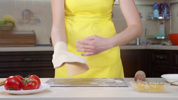 Woman Cook Throws Dough in Her Hands. Preparation of Pizza Dough. Woman in Yellow Clothes and