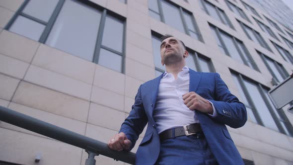 A Business Man in a Business Suit Adjusts His Suit Against the Background of an Office Building of a