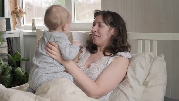 Mother Waking Up with Newborn Playing on Bed