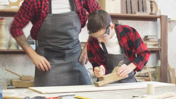 Carpenter Watching His Little Trainee Working with Jointer at the Wooden Table