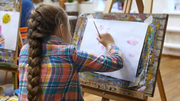 Young Cute Female Artist Is in an Art Studio, Sitting Behind an Easel and Painting on Canvas