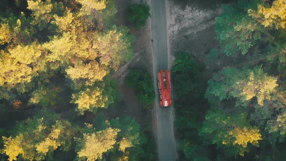 Top View From the Drone To the Red Fire Truck Driving Along the Road in a Pine Forest