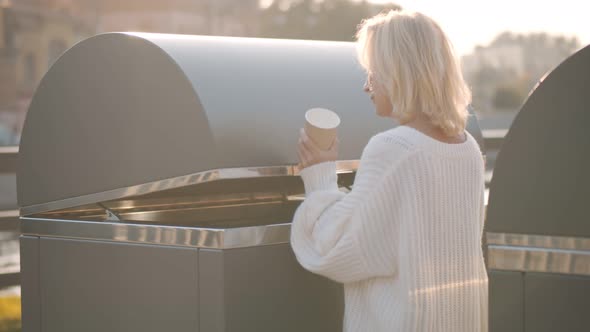 Portrait of Aged Woman Throwing Paper Cup in Large Trash Can Outdoors