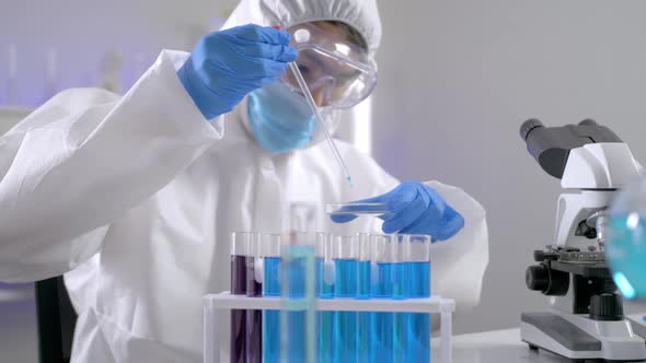 Scientist in PPE suite doing some research checking a liquid in a test tube at laboratory.