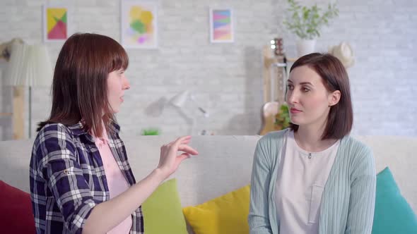 Two Beautiful Deaf Young Women Talking With Sign Language in the Living Room at Home