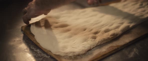 Chef preparing traditional italian al taglio pizza dough on a wooden surface.