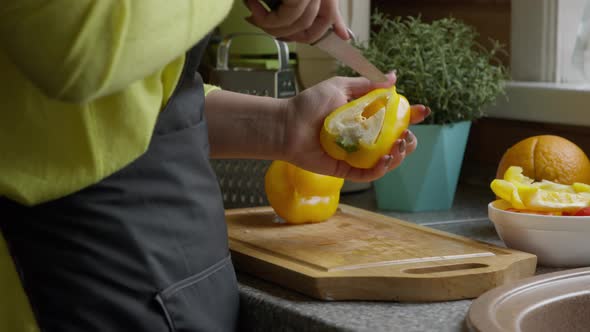 Housewife Cuts Yellow Sweet Paprika with Sharp Kitchen Knife on Oak Board