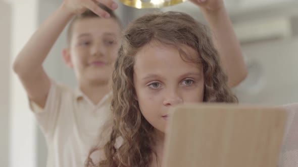 The Boy Putting the Crown on the Head of Curly Girl Looking in the Mirror. The Crown Is Too Big for