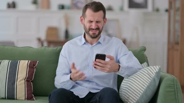 Young Man Reacting To Loss on Smartphone on Sofa 