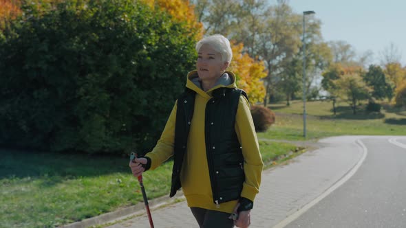 Shot of Woman Walking in Sunny Fall Park with Nordic Walking Sticks Front View