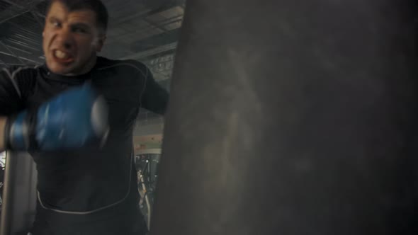 Side View of Young Caucasian Athlete Wearing Punching Punching Bag in Modern Gym