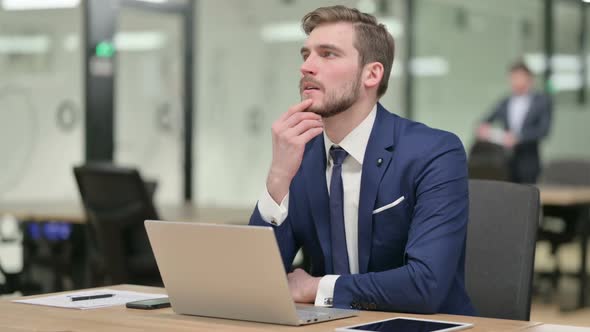 Young Businessman with Laptop Thinking at Work