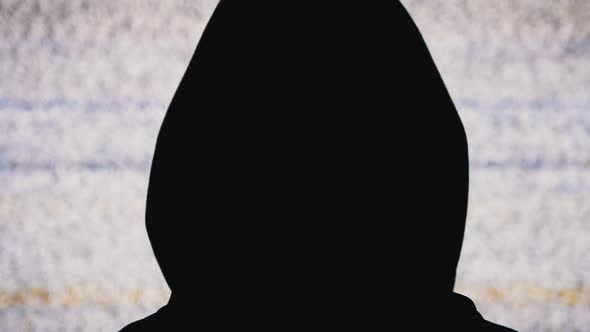 Silhouette of Man's Head in Hood Is Watching White Static Noise and TV Interference.