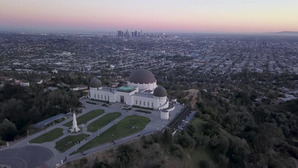 Aerial flying away from the Griffith Observatory in the evening and the Los Angeles city skyline.