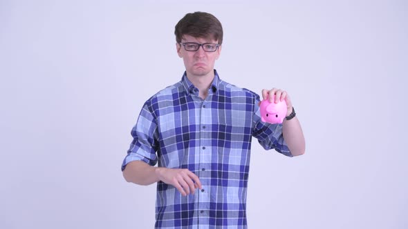 Stressed Young Hipster Man Holding Piggy Bank and Giving Thumbs Down