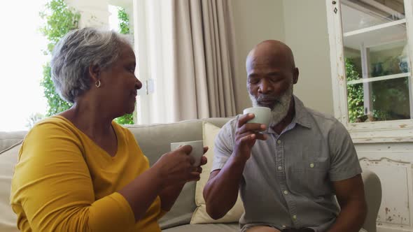 African american senior couple smiling while having coffee together sitting on the couch at home