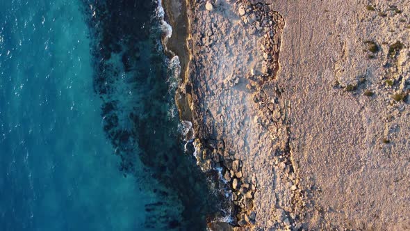 Flying Over Rocky Coastline Alongside Cliffside with Blue Mediterranean Sea Ocean Water Towards the