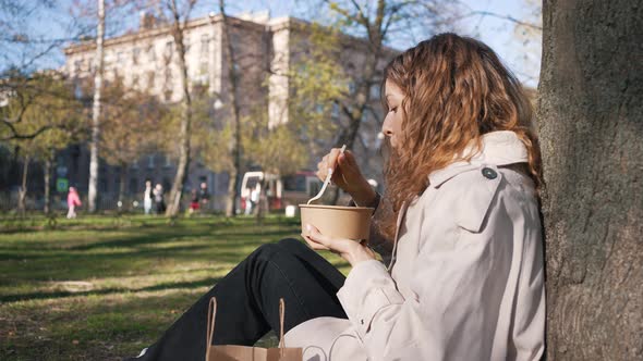 Cute Young Woman Eats Lunch From a Cardboard Plate in a City Park During Lunch Break