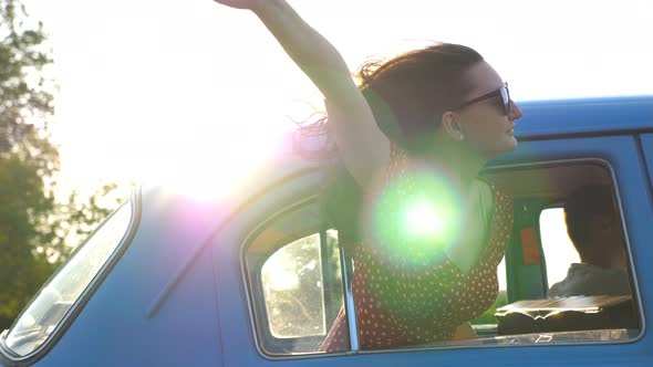 Young Woman Looking Out Window of Moving Old Auto. Happy Girl in Sunglasses Leaning Out of Retro Car