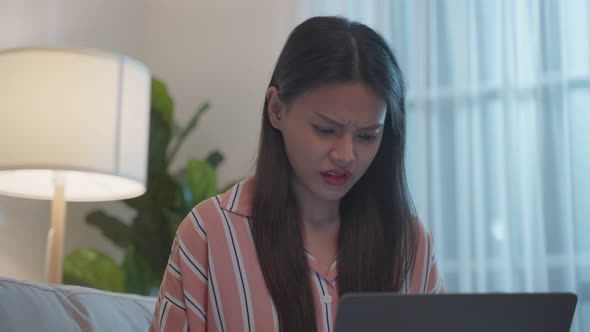 Asian beautiful girl typing on laptop keyboard in living room at night.