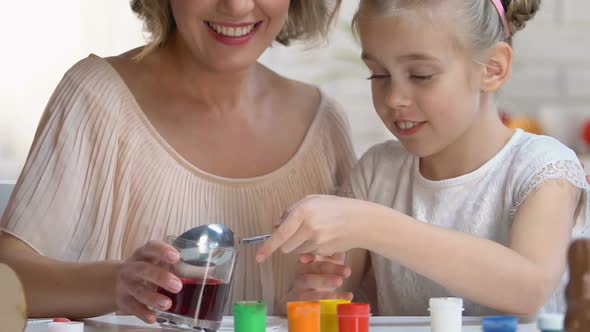 Girl in Funny Headband Putting Egg Into Red Food Coloring, Easter Traditions