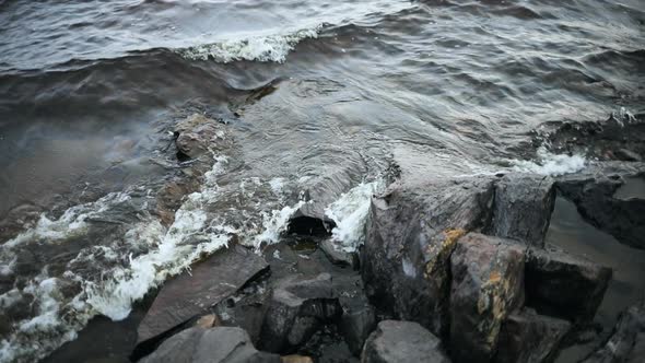 Handheld view down on waves hitting cliffs, on a rocky shore, on a cloudy autumn day, in Finland