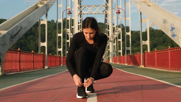 Woman Tying Shoelace on Sneakers on City Bridge and Starting To Run. Female Athlete Ties Running