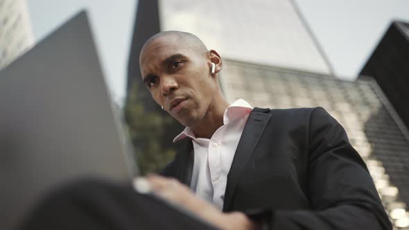 Displeased African businessman working on laptop and talking in headphones