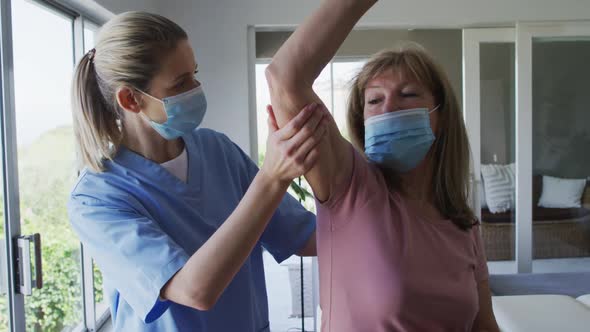 Female health worker assisting senior woman to exercise with dumbbells at home