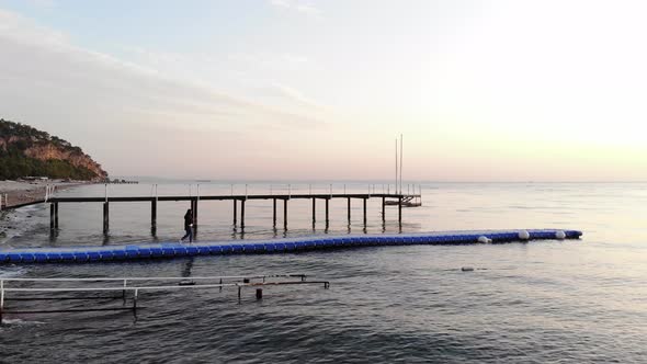 Aerial View of Young Girl Going From the Mountainous Coast on Plastic Modular Pier in Calm Sea