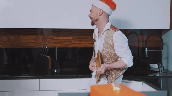 Handsome Young Man with Santa Hat Wiping Choping Board Like He is Playing Guitar