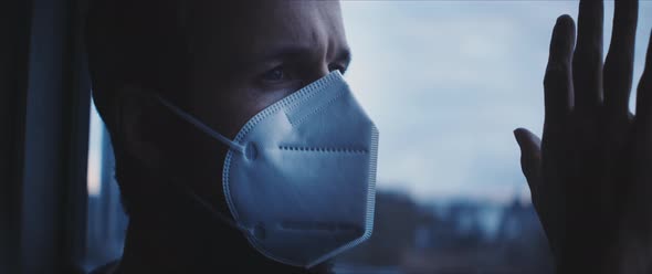 Man wearing a face mask and standing behind a window looking at a person's hand touching the glass