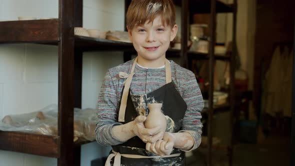 Portrait of Joyful Boy Young Potter Holding Hand-made Vase in Workshop Standing Alone Smiling